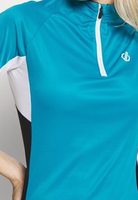 Tyrkysový sportovní top s půlzipem a žebrovanou strukturou. Má bílé akcenty na límci a černé boční panely.