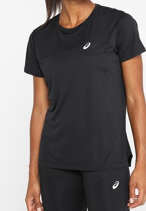 Vrouw die een zwart sportshirt met korte mouwen en een broek draagt met witte Asics-logo's op de borst en het bovenbeen.