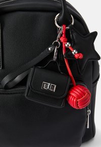 Mochila preta de couro com superfície texturizada, acessórios em prata, chaveiro com destaque em vermelho e uma pequena bolsa preta anexada.