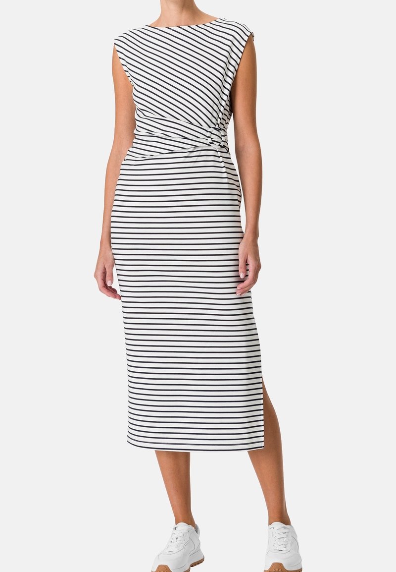 Robe midi blanche sans manches avec des rayures horizontales noires et une fente latérale, portée avec des baskets blanches par une femme debout.