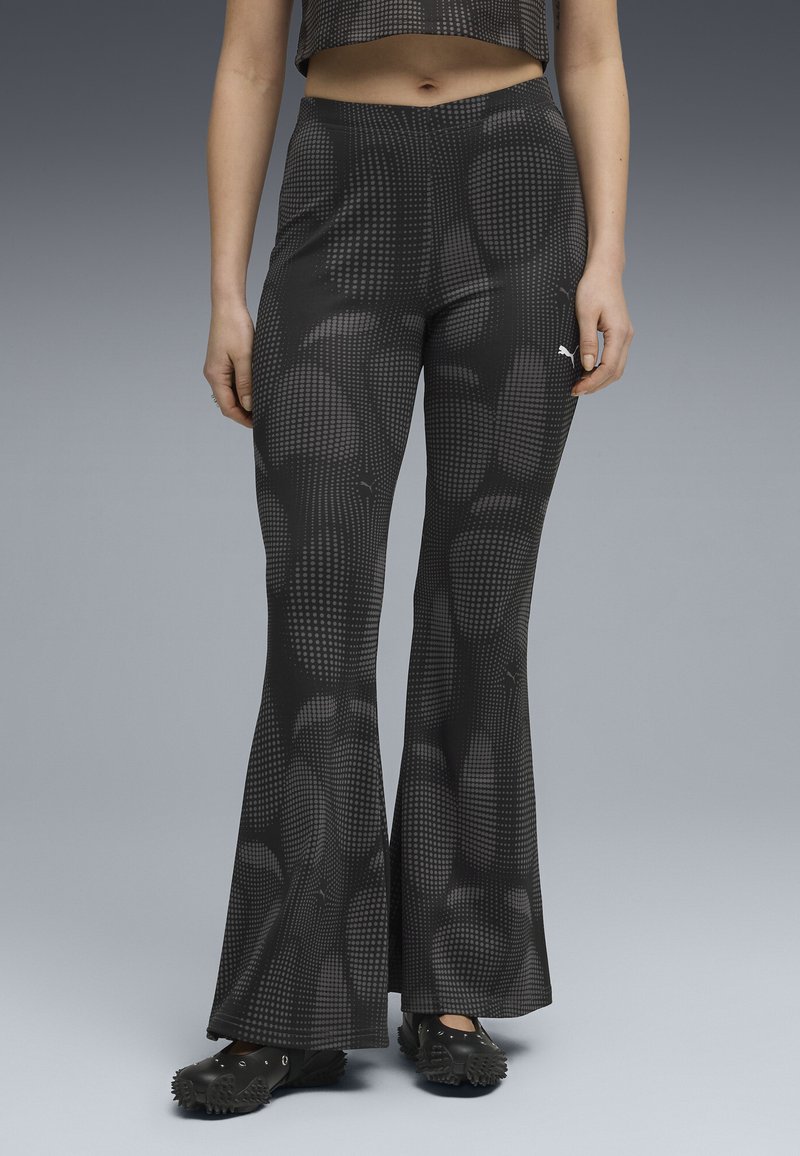 Black flared pants with a textured dot pattern. Material appears stretchy, featuring a high waistband and a small white brand logo on the side.