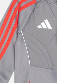 Gray sports jacket featuring red stripes, white accents, and the Adidas logo. Material appears textured with quilted detailing.