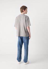 Grå oversized t-shirt med korte ærmer, parret med blå jeans. Stoffet ser glat og afslappet ud. Skoene er hvide, hvilket fuldender outfittet.