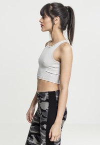 Svetlo siva skrajšana majica brez rokavov v kombinaciji z črno-sivimi kamuflažnimi leggings. Tkanina se zdi gladka, z oprijetim dizajnom in visokim pasom.