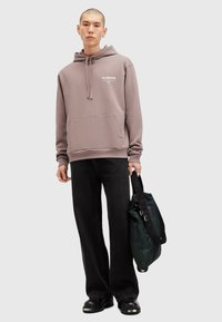 Grå hættetrøje med kængurulomme og snor, sorte vide jeans, sorte platform sko og en grøn mønstret skuldertaske.