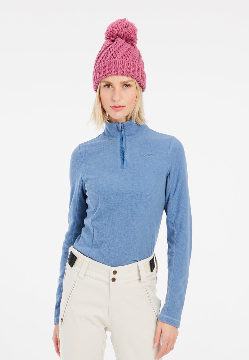 Lyseblå fleecepullover med høj krave og lynlås. Parret med off-white bukser med en sort og brun linning. Lyserød strikket hat.