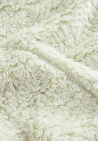 Gros plan d'un tissu polaire doux, duveteux et blanc cassé avec des coutures visibles le long d'une ligne de couture.