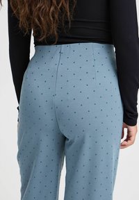 Lichtblauwe broek met stippen, gemaakt van een gladde stof, met een aansluitende taille en wijde benen, gecombineerd met een zwart T-shirt met lange mouwen.