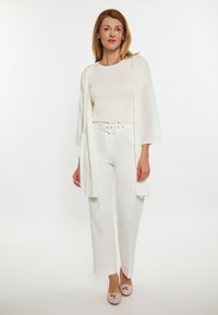 Cardigan leggero a maniche lunghe di colore bianco, abbinato a una maglia aderente bianca e pantaloni a gamba larga. Presenta un girovita con cintura e scarpe beige.