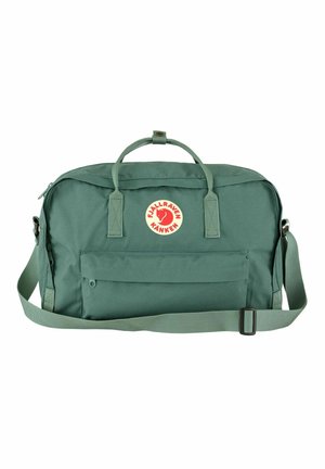 Sac de sport en tissu vert avec deux poignées supérieures, une bandoulière réglable, une poche zippée à l'avant et un écusson de logo circulaire à l'avant.