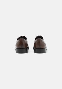Pantofi din piele maro cu vârf rotunjit, textură netedă și detalii de cusătură minime. Talpa din cauciuc este elegantă și ușor ridicată.