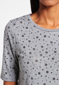 Camiseta gris de manga corta con un patrón de puntos dispersos en varias tonalidades de gris. Tejido suave con escote redondo.