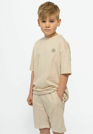 Beige katoenen t-shirt en short set, ontspannen pasvorm, ronde halslijn en een klein circulair logo op de borst. Zachte textuur en casual ontwerp.