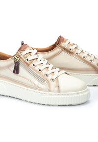 Zapatillas de cuero beige con acentos metálicos, un patrón texturizado, cordones blancos y un cierre lateral con cremallera. Presentan una suela blanca gruesa y estriada.