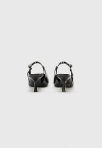 Tacones de slingback negros hechos de cuero sintético texturizado, con un tacón estrecho y una correa para el tobillo con un detalle de hebilla en tono dorado.