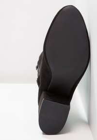 Botte en daim noir avec une semelle en caoutchouc texturée et un talon bas. Comprend une fermeture éclair latérale et une finition lisse sur la tige.