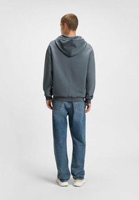 Hoodie van donkergrijze stof, gecombineerd met losse blauwe jeans. De outfit heeft een eenvoudig ontwerp met ribbelmanchetten en -zoom.
