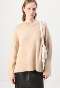 Lys beige genser laget av myk strikket stoff, med en ribbestrikket kant og mansjetter. Kombinert med en liten kremfarget crossover-veske og svarte lærbukser.