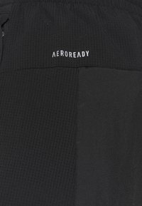 Schwarze sportliche Shorts aus strukturiertem Stoff mit Perforationen und einem glatten Abschnitt, mit der Aufschrift "AEROREADY" in Weiß am Bund.