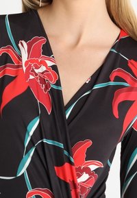 Svart omlottklänning med stora röda blommönster och turkosa detaljer. Slätt tyg med v-ringning och överlappande framdesign.