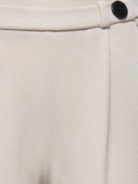 Κοντινή λήψη στη μέση μίας μπεζ υφασμάτινης παντελόνας με μαύρο κουμπί και λεπτομέρειες θηλιών ζώνης.