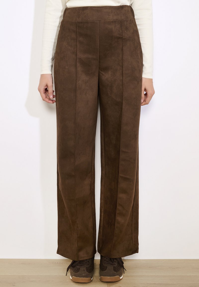 Brązowe, wysokie spodnie wykonane z miękkiego materiału przypominającego zamsz, o prostym kroju nogawki z plisami z przodu oraz gładkiej teksturze.