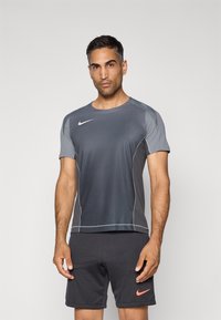 Grå kortermet Nike treningsskjorte med rund hals, kontrasterende gr�å skulderpaneler og reflekterende sømmer. Bært med mørke shorts.