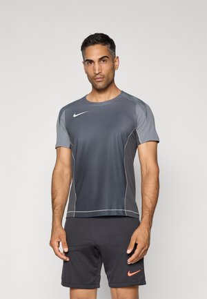 Grå kortærmet Nike sportsskjorte med rund halsudskæring, kontrasterende grå skulderpaneler og reflekterende sømme. Bæres med mørke shorts.