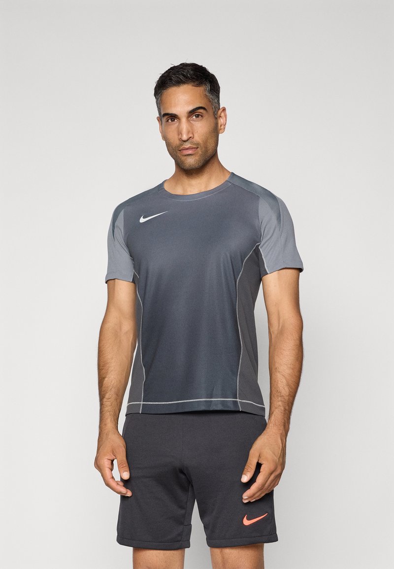 Grå kortermet Nike treningsskjorte med rund hals, kontrasterende grå skulderpaneler og reflekterende sømmer. Bært med mørke shorts.