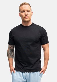 T-shirt nera in cotone con maniche corte, scollo rotondo e una consistenza liscia. Presenta un design aderente e un dettaglio logo discreto.