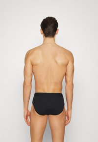 Culottes en coton noir avec une texture lisse, dotées d'uneLarge ceinture et d'une coupe classique. Le design est simple et fonctionnel.