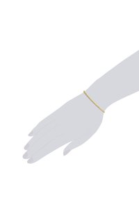 Zlatna narukvica na sivim rukama. Narukvica ima delikatnu, glatku teksturu s okruglim karikama, dizajnirana za usko pristajanje.