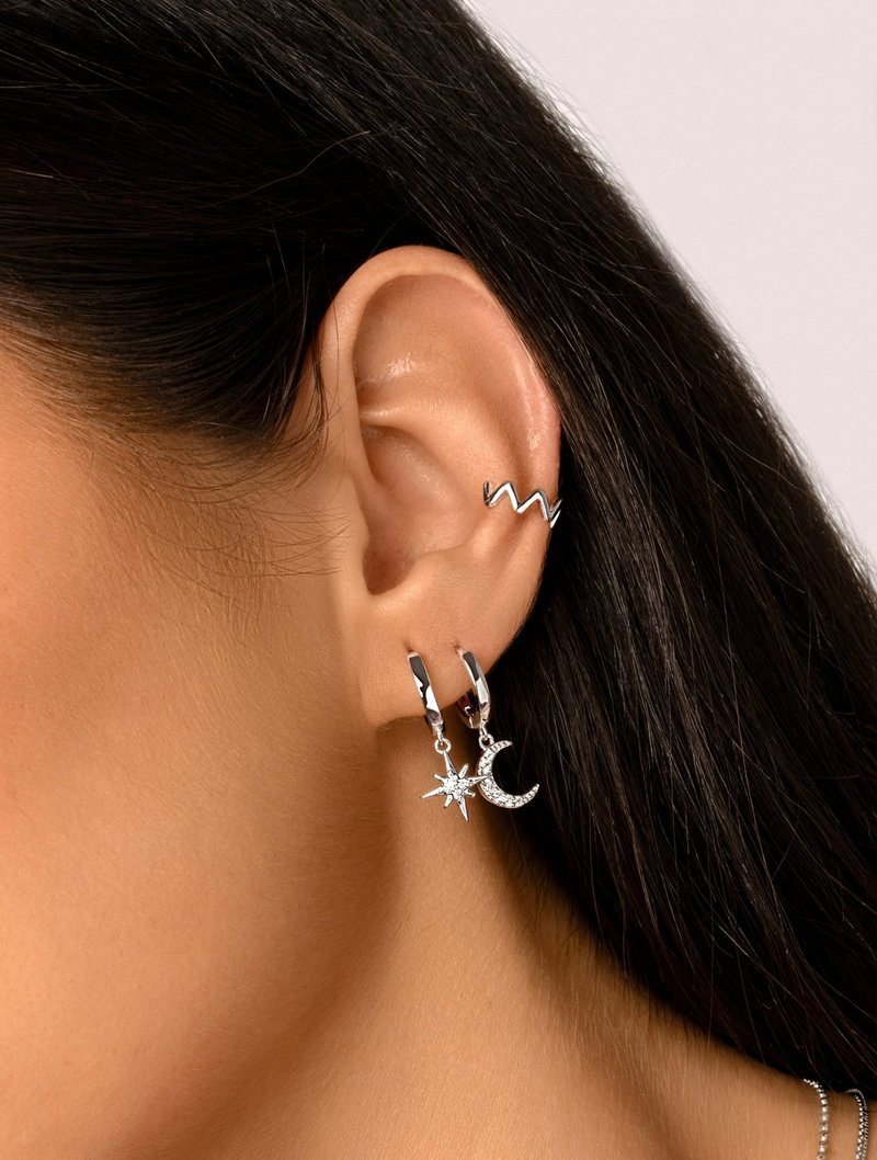 Orecchini a cerchio in argento con un charm a stella e luna crescente. Presentano un accento a zigzag testurizzato sulla parte superiore dell'orecchio. I charm hanno una finitura lucida.