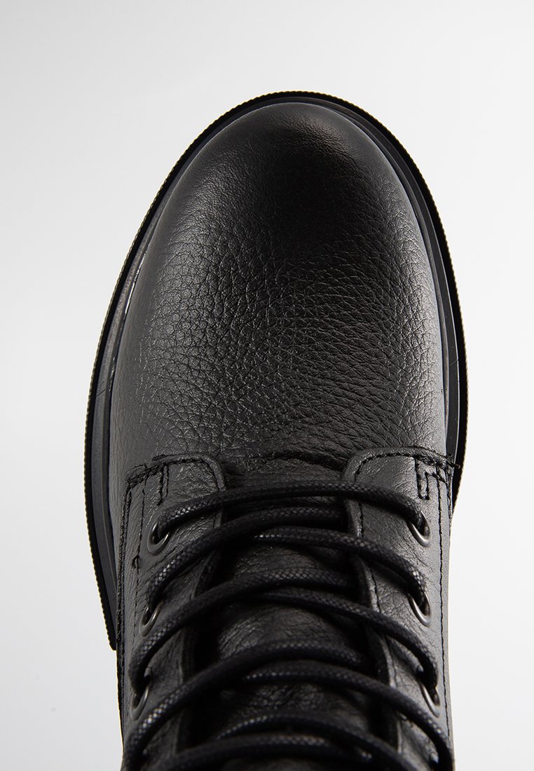 Czarny skórzany but z teksturową powierzchnią, zaokrąglonym czubkiem, sznurowaniem z przodu oraz gumową podeszwą. Projekt jest minimalistyczny i funkcjonalny.