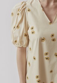 Robe à manches bouffantes en coton jaune clair. Présente des imprimés de tournesols éparpillés en marron et noir. Design à col en V avec des détails froncés aux épaules.