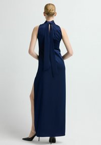 Granatowa sukienka na szyję z wiązaniem z tyłu i wysokim rozcięciem. Wykonana z gładkiej tkaniny, charakteryzuje się smukłym krojem i długością sięgającą podłogi.