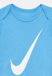 Body azul de algodão com um grande logótipo Nike Swoosh branco. Mangas curtas, gola redonda e textura suave.