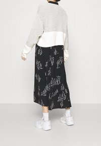 Maglione grigio e bianco tagliato su una gonna nera con disegni in linea bianca di figure, abbinato a sneaker bianche e calze alla caviglia.