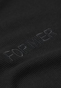 Black textured fabric displaying the word "FORMER" in stitched embroidery. The surface is slightly raised with a woven pattern.