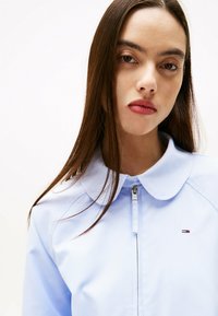 Giacca zip-up azzurro chiaro con colletto rotondo e piccolo logo sul petto. Presenta una texture liscia e un design aderente.