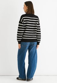 Black and white striped knitted sweater with a round neckline, ribbed cuffs, and hem, paired with loose blue denim jeans.