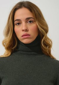Grüner gerippter Rollkragenpullover aus weichem Strickmaterial. Verfügt über einen hohen Kragen und ein figurbetontes Design, das Textur und Struktur betont.