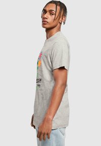 Grå bomulds t-shirt med et farverigt blomsterprint på fronten, rund halsudskæring og korte ærmer. Model vist i profil.