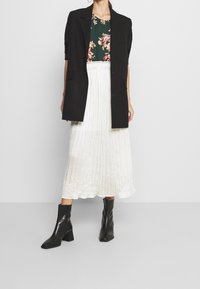 Černý přiznaný sako, květinový zelený top, bílá plisovaná midi sukně a černé kotníkové boty na blokovém podpatku. Jednoduchý design, hladké textury.