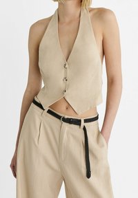 Beżowy top na szyję z głębokim dekoltem w kształcie litery V, o kroju krótkim, z trzema guzikami z przodu. Połączony z beżowymi spodniami z wysokim stanem i plecionym czarnym paskiem.