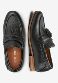 Svarta loafers med ett strukturerat ovansidan, en mjuk läderrem och en rosett, brun gummisula och vadderad innersula för komfort.