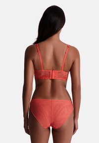 Ensemble de lingerie corail comprenant un soutien-gorge en dentelle transparente avec dos en dentelle et bretelles ajustables, accompagné de culottes taille haute assorties. Texture lisse avec des accents floraux.