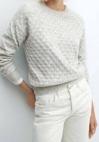 Pull en maille gris clair avec un motif texturé et un col côtelé, associé à un jean en denim blanc. Le pull a des manches longues et une coupe décontractée.