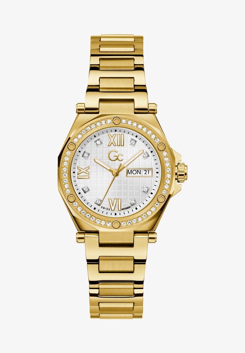 Kuldtooni kellok, millel on oktaadiline korpus, valge tekstureeritud kellanägu, rooma numbrid, kuupäeva näidik ning kristallaktsentidega bezel ja kellanägu. Metallist ketiga rihm.