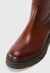 Braune Leder-Ankle-Boots mit glatter Oberfläche, runder Spitze und strukturierter Gummisohle mit einem Zickzackmuster entlang der Kante.